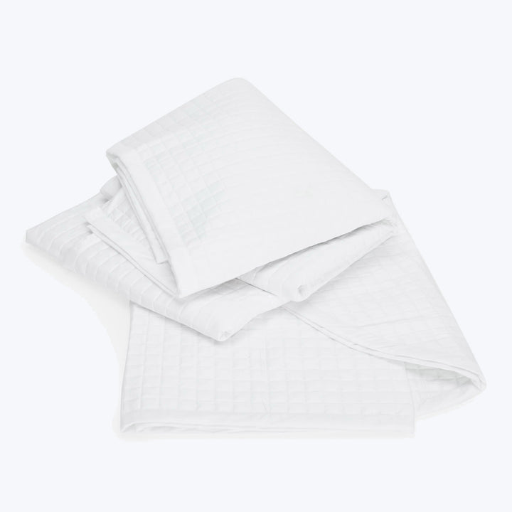 Neatly folded white bed linens with textured pattern stacked elegantly.