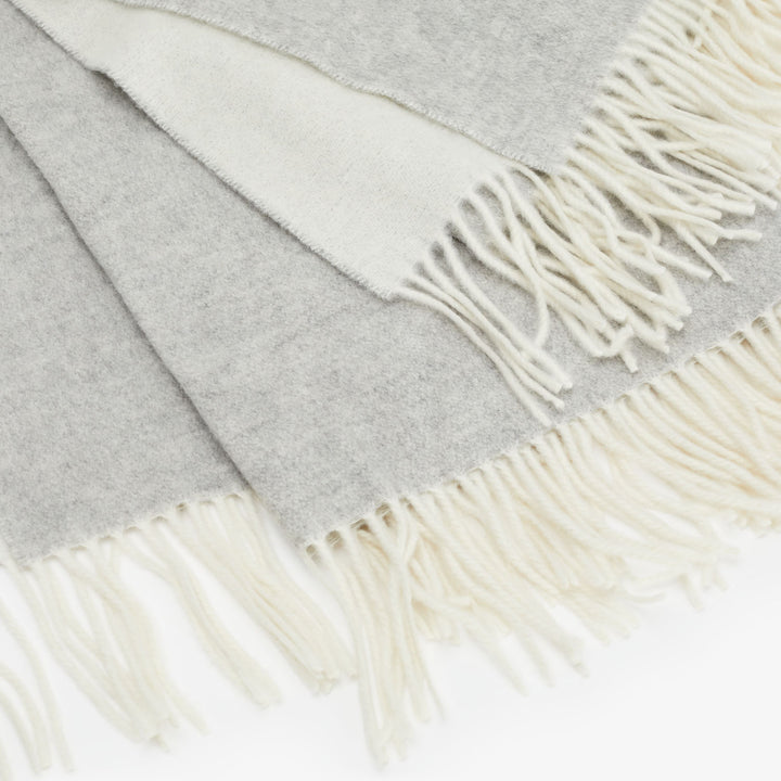 Close-up of gray textile with cream fringe, soft and warm.