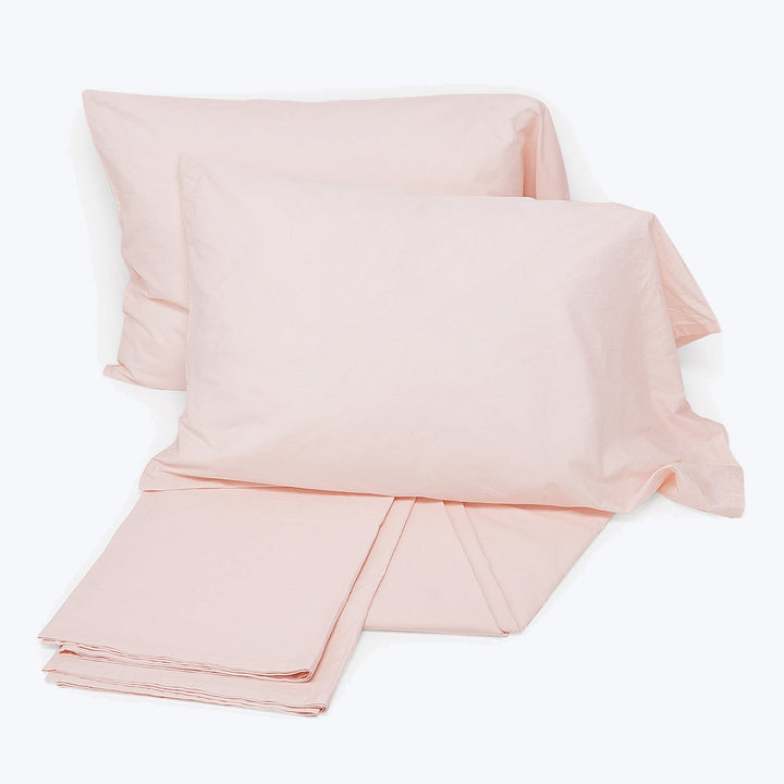 Light pink bed linens with two pillowcases on white background.