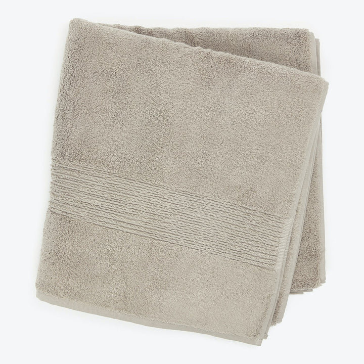 Beige bath towel with textured band, soft lighting, product image.