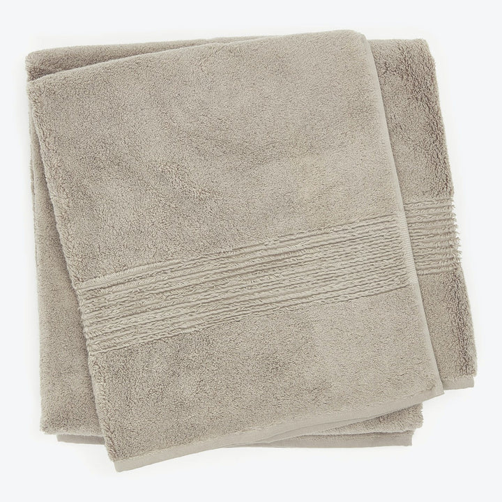 Folded plush beige towels with decorative patterned band stacked neatly.