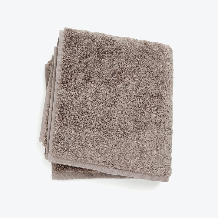 Plush taupe towel with fluffy texture against white background.