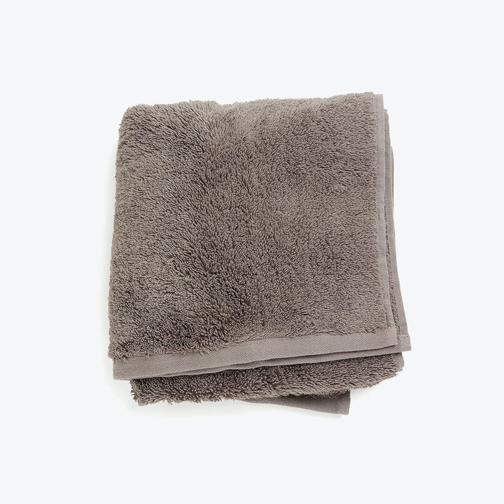 Folded gray plush towel on white background with neat hem.