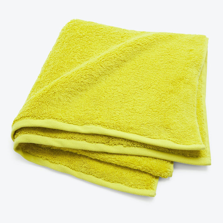 Vivid yellow terry cloth towel neatly folded on white background.