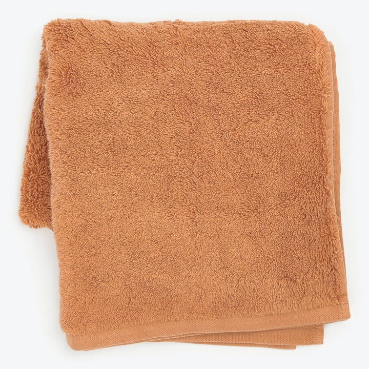 Folded terracotta-colored towel with plush terrycloth texture on white background.