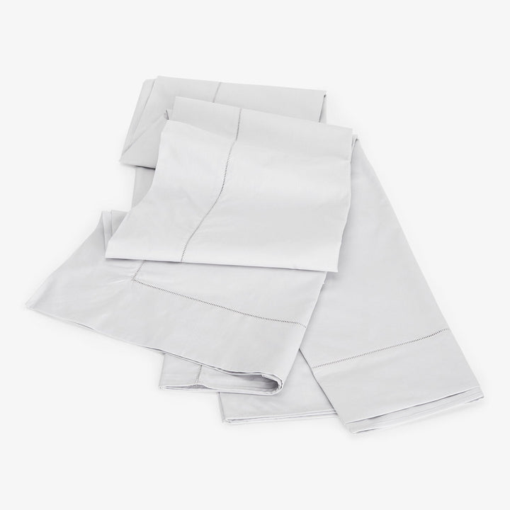 Neatly folded light grey bed sheets with elegant design detail.