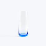 Empty tall glass with blue base against white minimalist background.