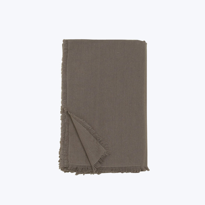 Folded linen throw in neutral earth tone with frayed edges.