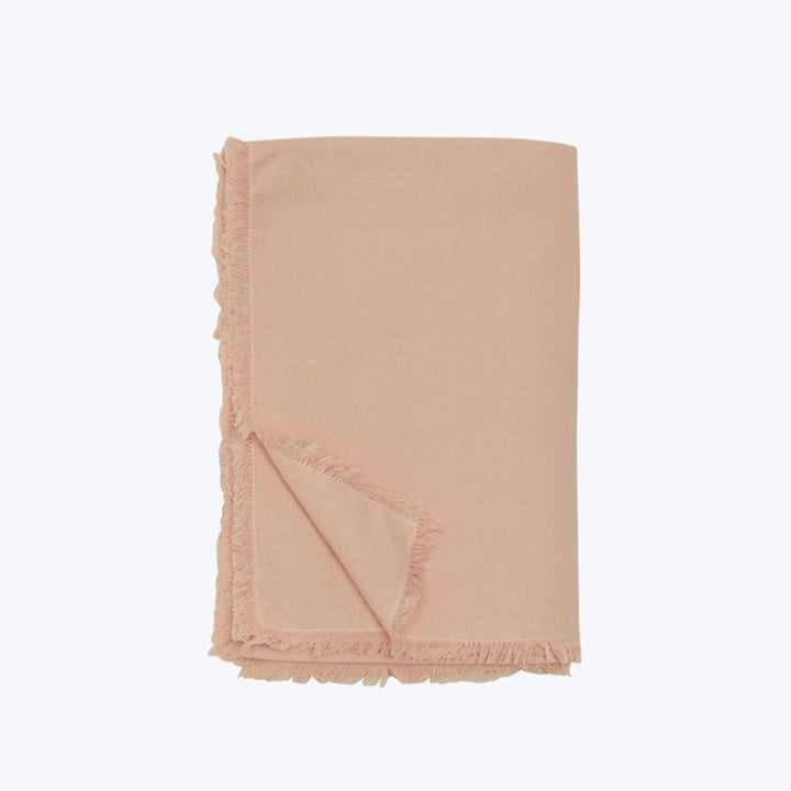 Peach throw blanket with fringe detail folded on white background.