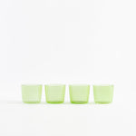 Four green translucent shot glasses arranged in a straight line.