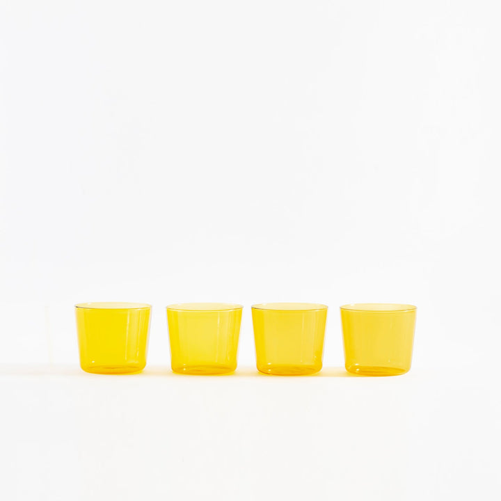 Four small yellow cups filled with liquid on white background