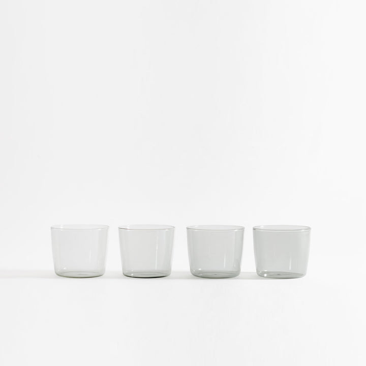 Row of four identical transparent drinking glasses on white background.