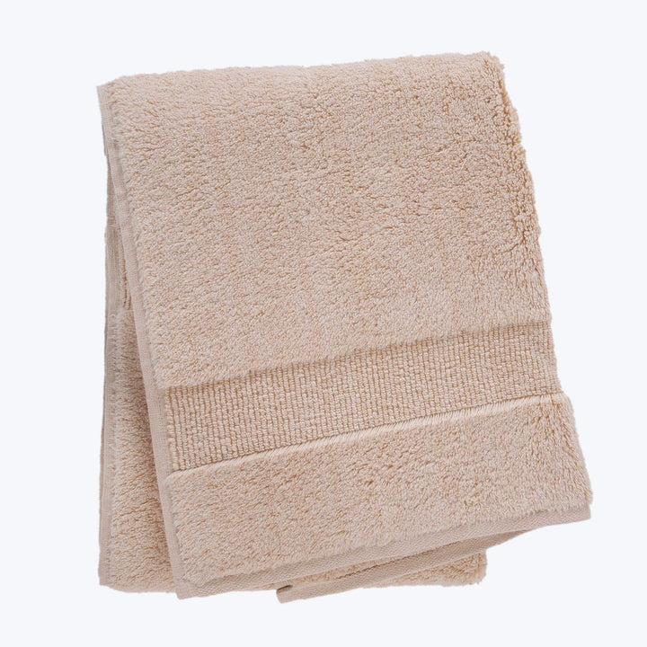 Neatly folded beige bath towel with decorative ribbed border design.