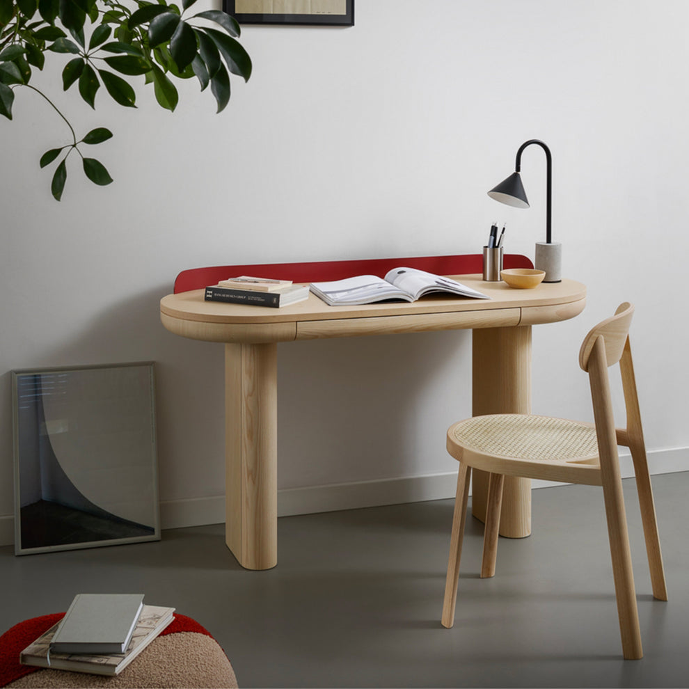 Minimalist office setup with wooden desk, chair, plants, books, and lamp.