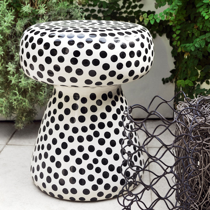 Modern mushroom-shaped stool with black dots, wire ornament, lush plants.