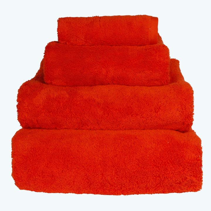 Set of fluffy red-orange bath towels stacked by size.