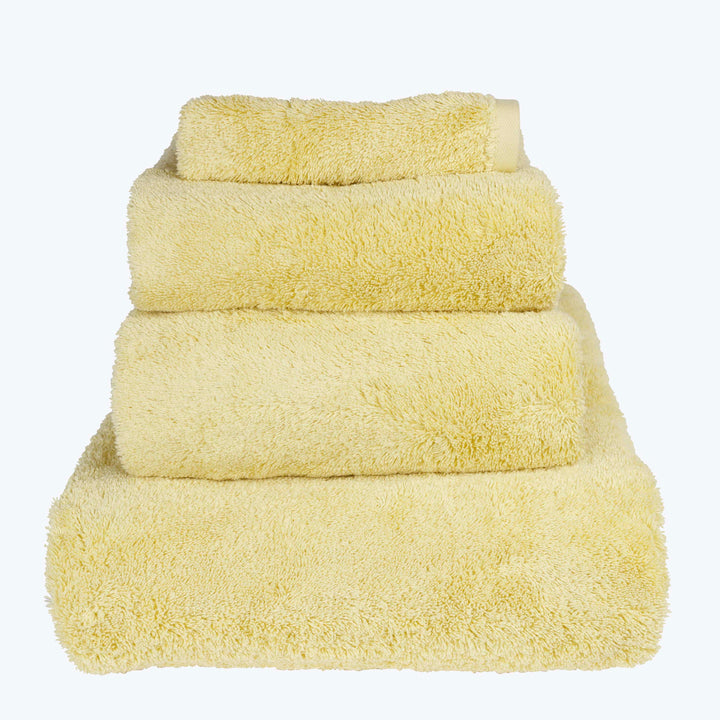 Neatly stacked pale yellow towels of different sizes on white.