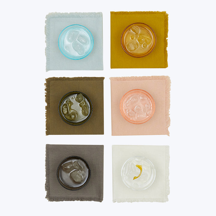 Artisanal cosmetic creams displayed on colored fabric squares, minimalist design