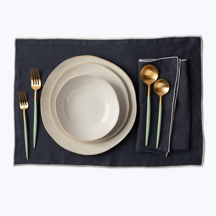 Elegant table setting with speckled plates and gold cutlery.