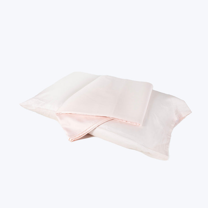 Two folded pillowcases in pink and white against white background.