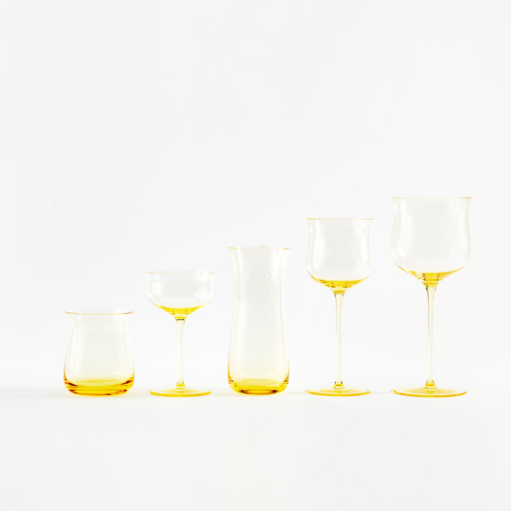 Five modern yellow-tinted glass vessels for serving wine or cocktails.