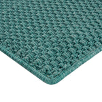 Close-up of teal/green woven rug with intricate loop & knot pattern.