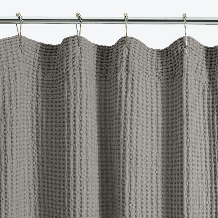 Gray knitted curtain with textured pattern hangs on curtain rod.
